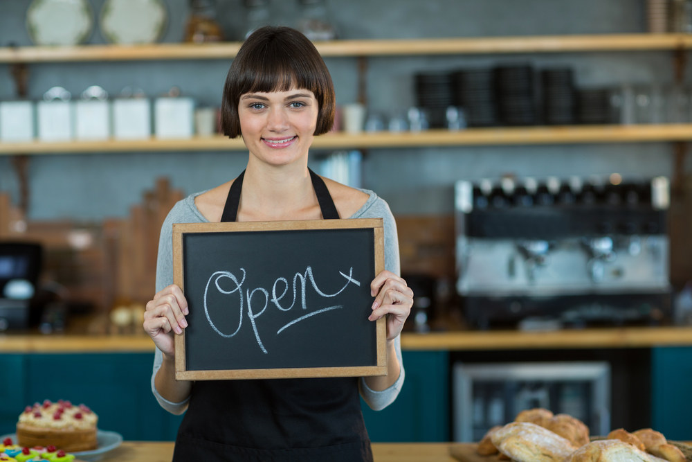 Portrait of smiling waitress showing slate with open sign in cafe